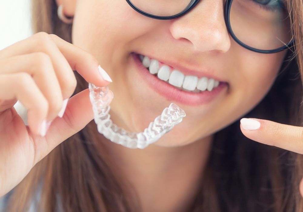 A lady holding an Invisalign, clear plastic aligner.